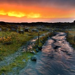 View of stream along landscape at sunset