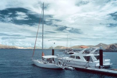 Boats sailing in sea against cloudy sky