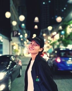 Portrait of smiling young woman standing on city street at night