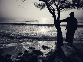 Silhouette man standing on rock at beach against sky