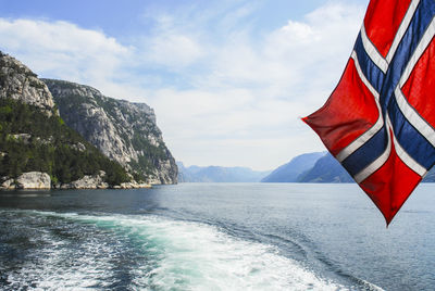 Norwegian flag over sea against mountains