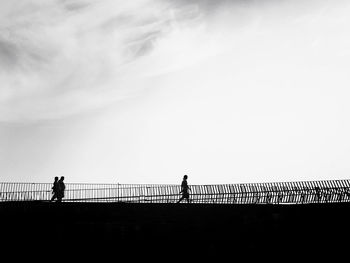 Silhouette people on railing at sunset