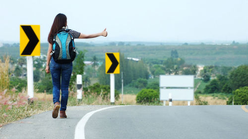 Rear view of woman hitchhiking on road