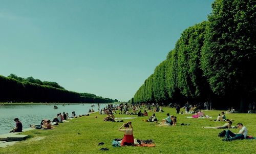 People relaxing on green landscape against clear sky