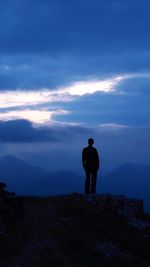 Silhouette man standing on cliff against cloudy sky