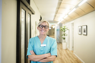 Portrait of mature female healthcare worker with arms crossed standing in hospital corridor