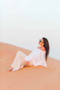 Side view of young woman sitting against wall