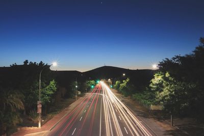 Light trails on road against clear blue sky at night
