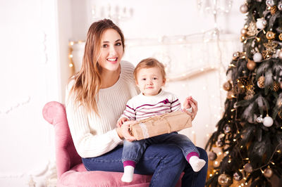 Portrait of woman with son holding gift box sitting on armchair
