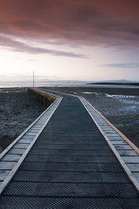 Pier over beach against cloudy sky during sunset