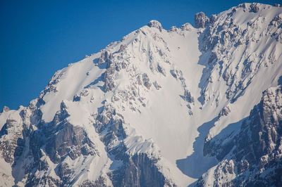 Low angle view of snowcapped mountains against clear blue sky