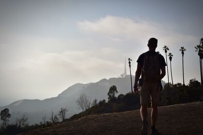 Rear view of man standing on mountain against sky