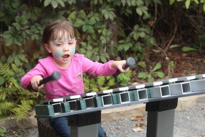 Cute girl with messy face playing xylophone against plants