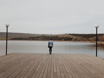 Rear view of woman standing on pier over lake against sky