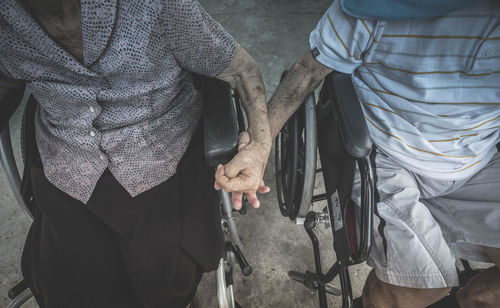 Midsection of couple sitting on wheelchairs holding hands