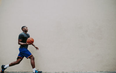 Young man playing basketball against wall