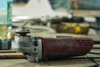 Close-up of a red dirty angle grinder. the tool without the safety guard is on the table in the shop