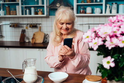 Smiling senior woman using smart phone in kitchen