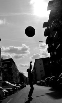 Side view of silhouette man catching ball on street during sunny day