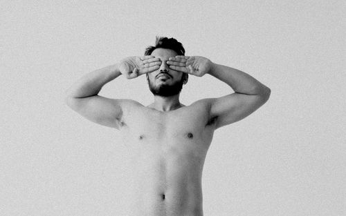 Shirtless young man covering eyes against white background