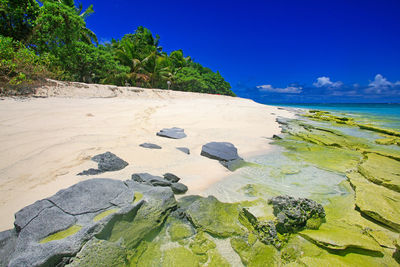 Scenic view of rocks on beach against blue sky