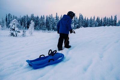 Rear view of boy pulling sleigh on snowy field