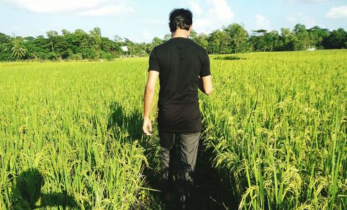 Rear view of man standing on field against sky