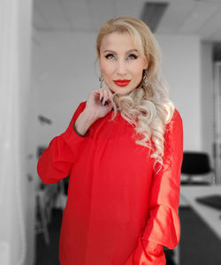 Portrait of young woman standing against red wall