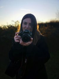 Portrait of young woman photographing on field