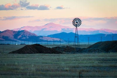 Wind turbines on land against pikes peak and sky during sunset