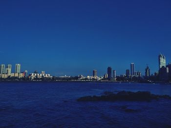 Sea by buildings against clear blue sky