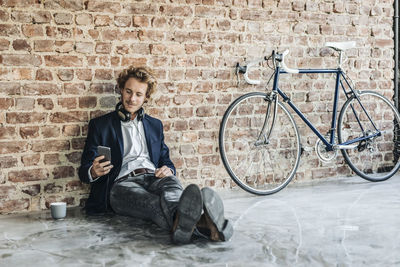 Man with headphones sitting on floor looking at cell phone