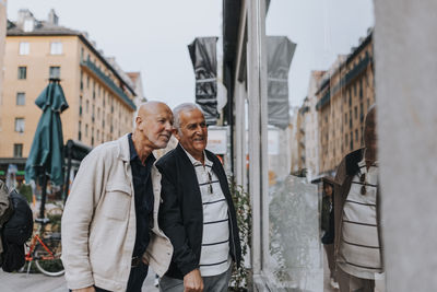 Senior male friends discussing with each other while doing window shopping at street