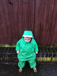 High angle view of boy wearing green raincoat against wooden fence