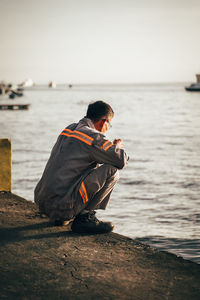 Side view of man sitting at beach against sky