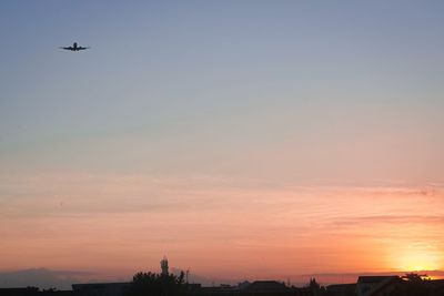 Silhouette airplane flying against sky during sunset