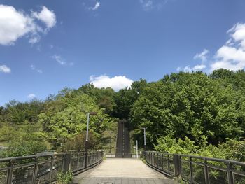 Footbridge amidst trees against sky