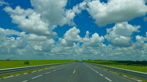 Road passing through field against cloudy sky