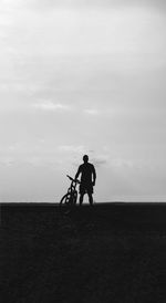 Silhouette man standing with bicycle on field against sky