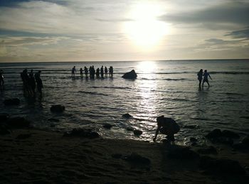 Silhouette people standing on beach against sky during sunset