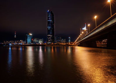 Illuminated city by river against sky at night