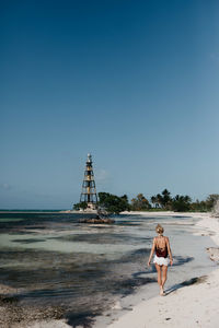 Rear view of woman walking on shore at beach against clear blue sky