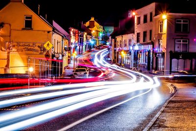 Light trails on road amidst buildings in city at night