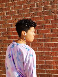 Young woman standing against brick wall on sunny day