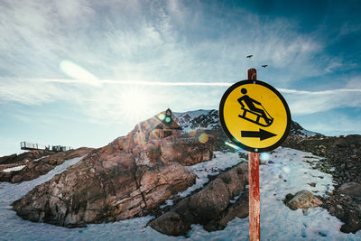 Road sign on snow covered mountain against sky