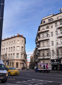 Cars on road by buildings against sky in city