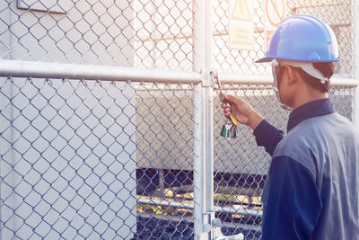 Male engineer opening padlock hanging from fence