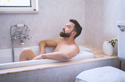 Side view of shirtless young woman sitting in bathroom