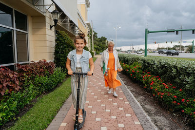 Portrait of happy senior women and granddaughter riding push scooter