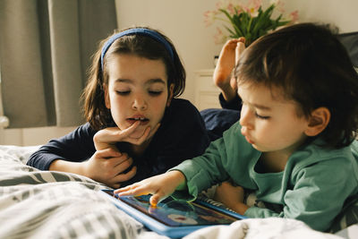 Brothers using digital tablet while lying together on bed at home